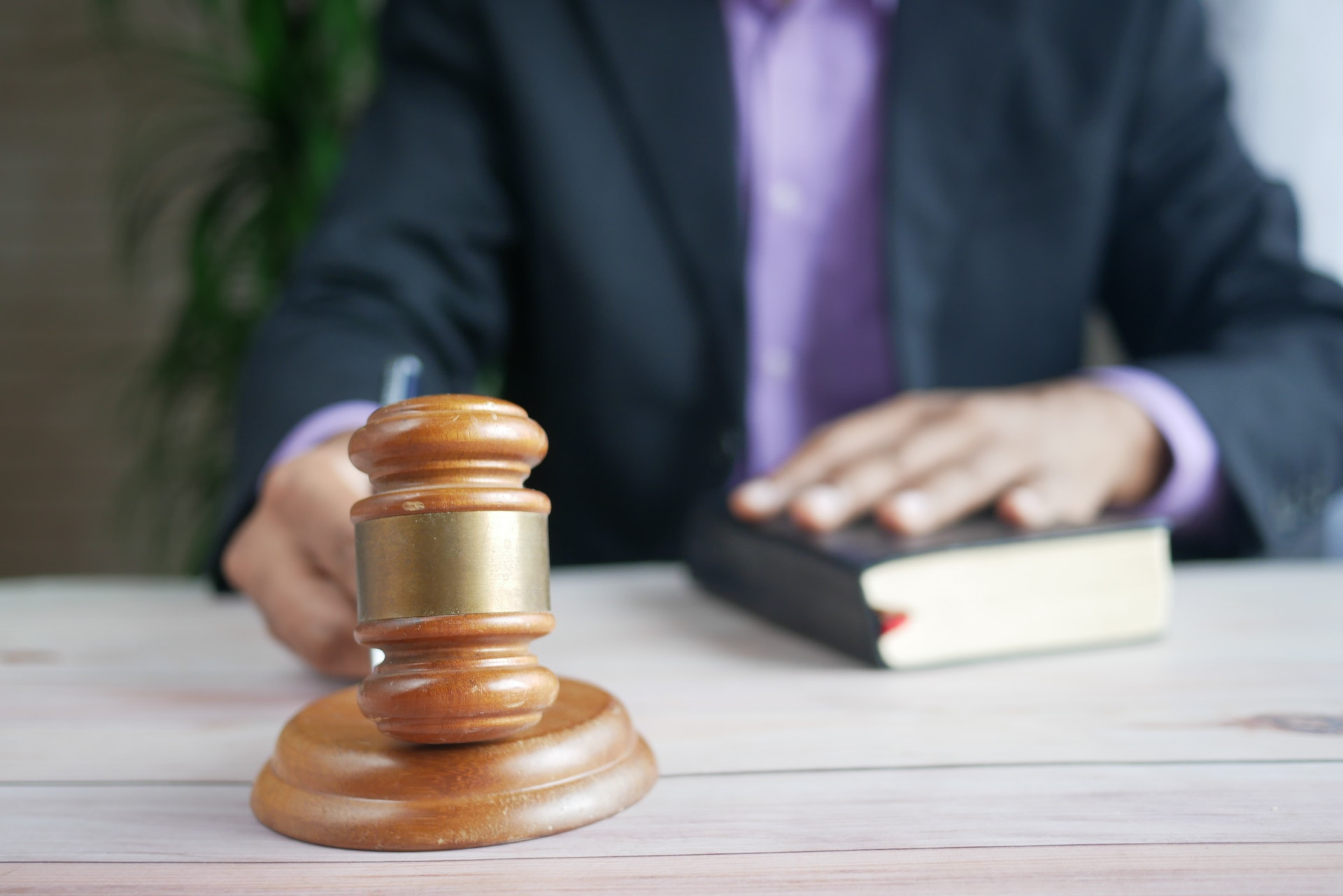 person holding a gavel with other hand resting on book