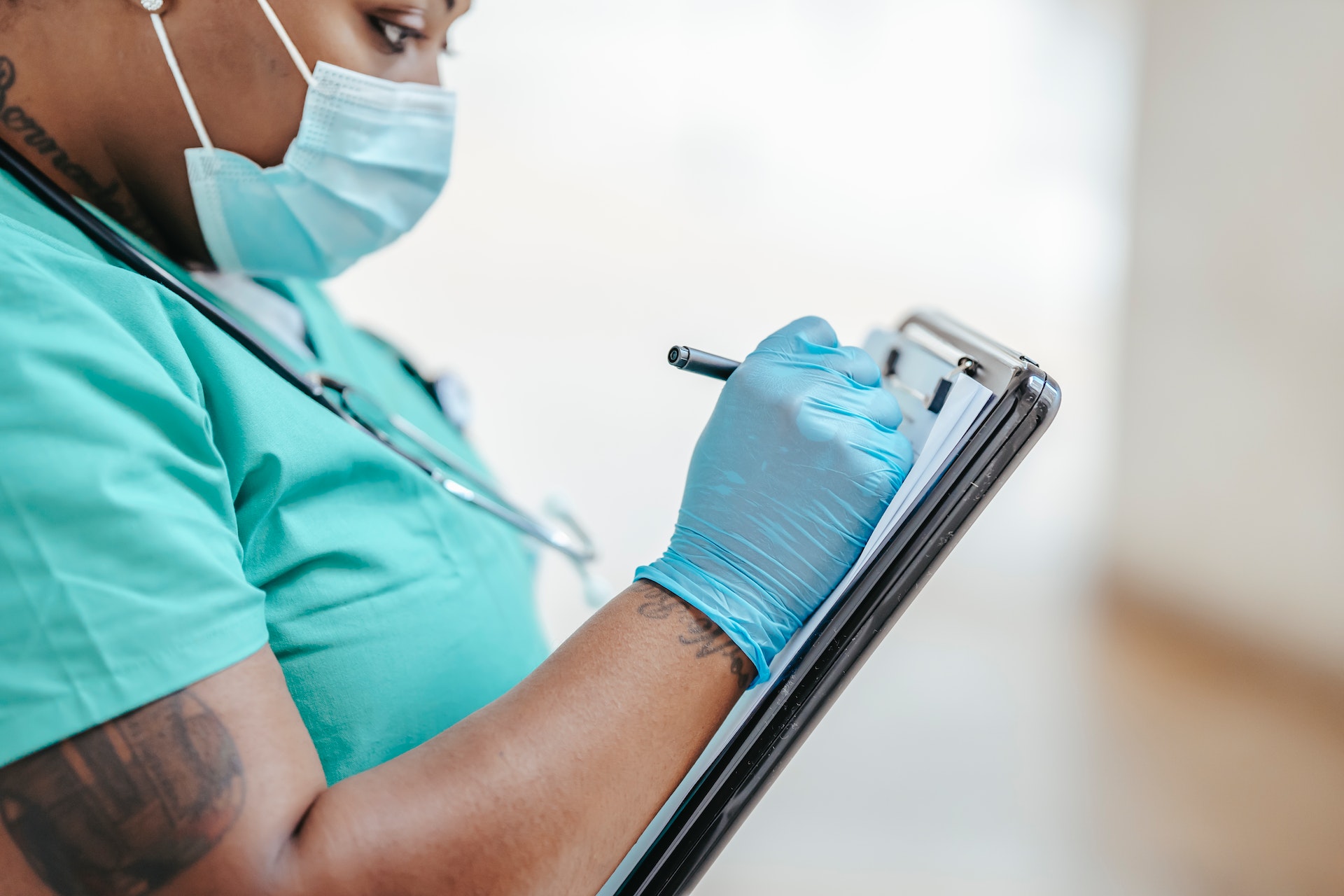 nurse with facemask and surgical gloves on writing on clipboard