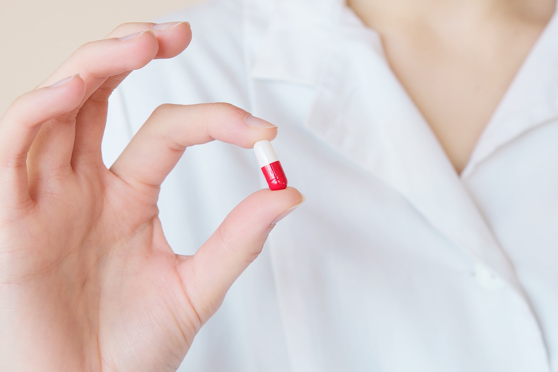person wearing white shirt holding a red and white pill between their pointer finger and thumb
